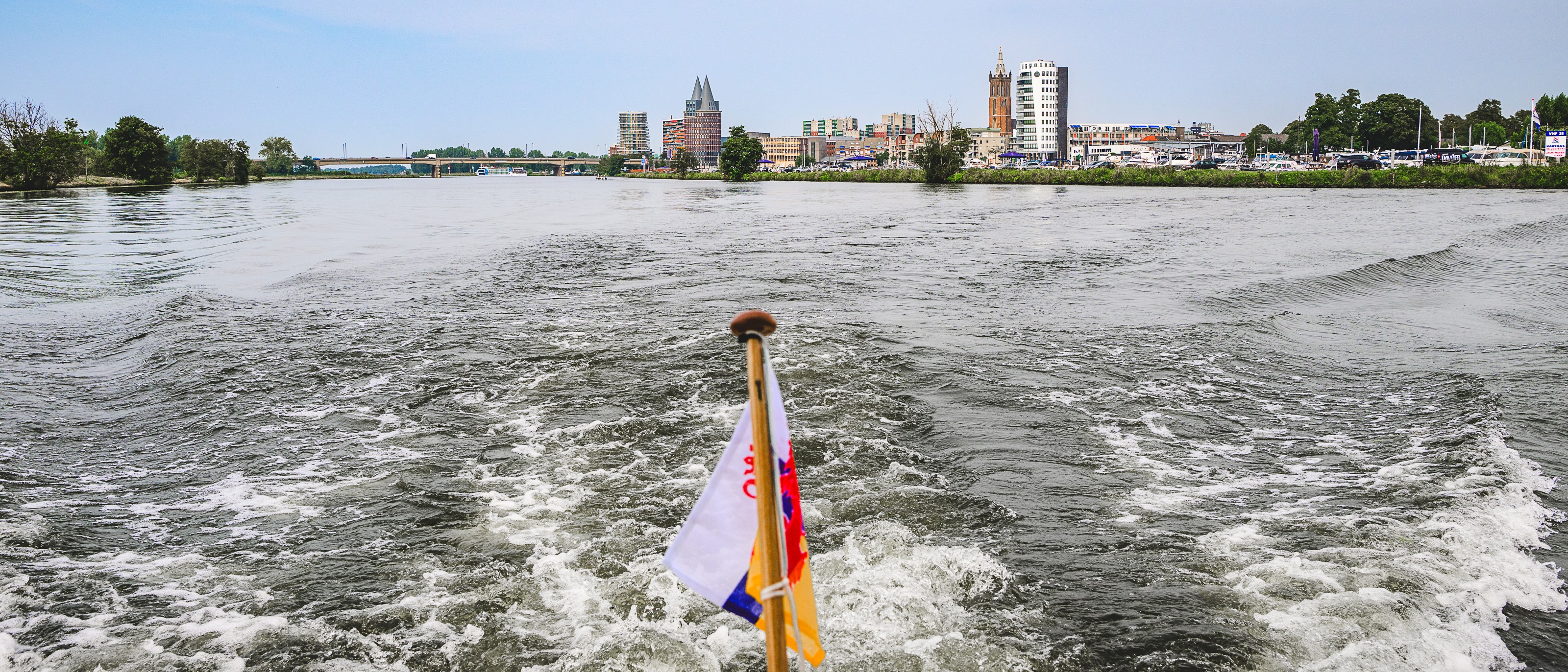 Uitzicht vanaf een varend schip op de Maasplassen met de skyline van Roermond op de achtergrond.