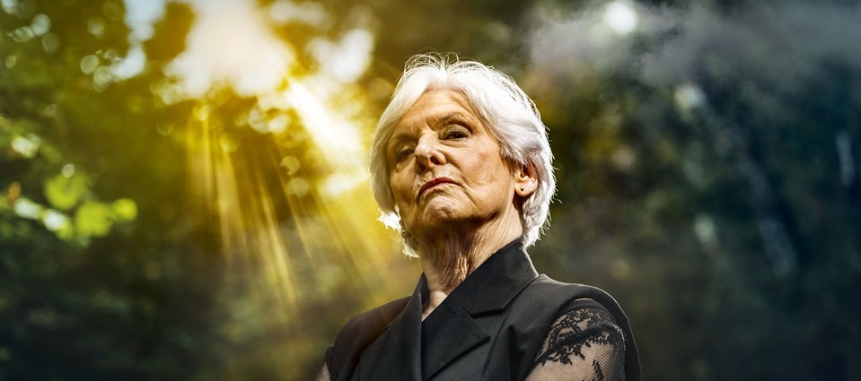 Vrouw met gekruiste armen in een bosachtig decor met zonlicht, scènebeeld van de Passiespelen Tegelen 2026.