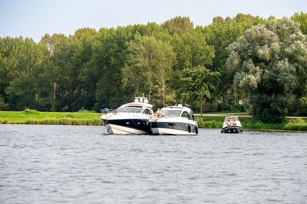 Drie motorboten liggen op de rustige Maasplassen met op de achtergrond een groene oever vol bomen.