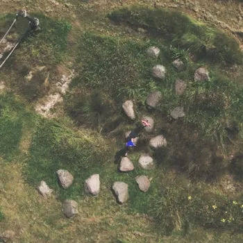 Bovenaanzicht van een kind dat speelt tussen grote stenen in een groen natuurgebied, met een volwassene op een wandelpad in de buurt.
