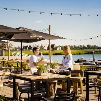 Gasten zitten op het zonnige terras van Humphrey’s in Thorn, met parasols, sfeerverlichting en uitzicht op het water.